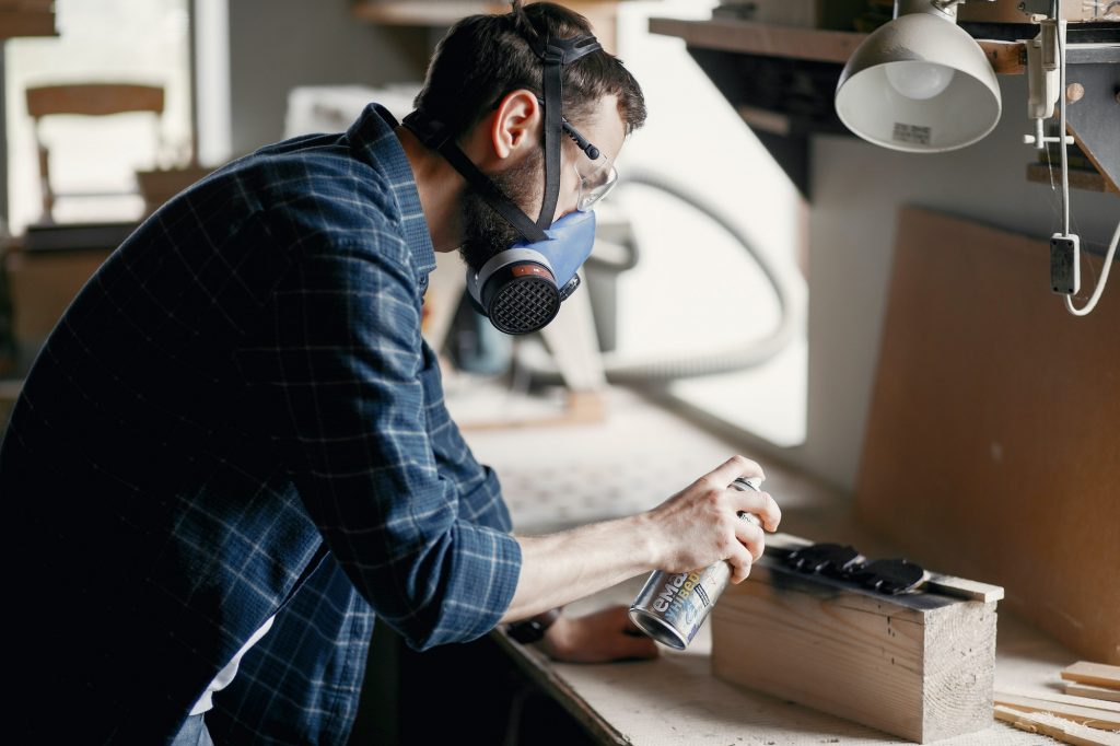 Man holding paint spray and painting wood